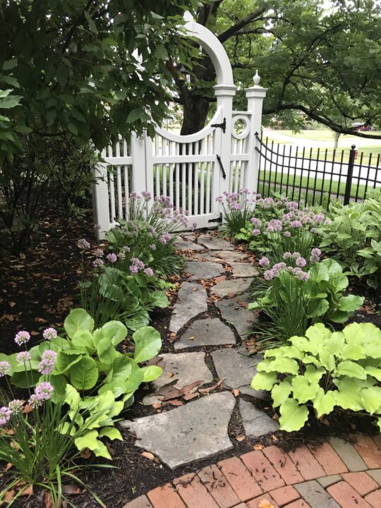 White picket fence and iron fence with a stone pathway give this backyard an English cottage garden vibe | Building Bluebird #cottagecore #grandmillennial